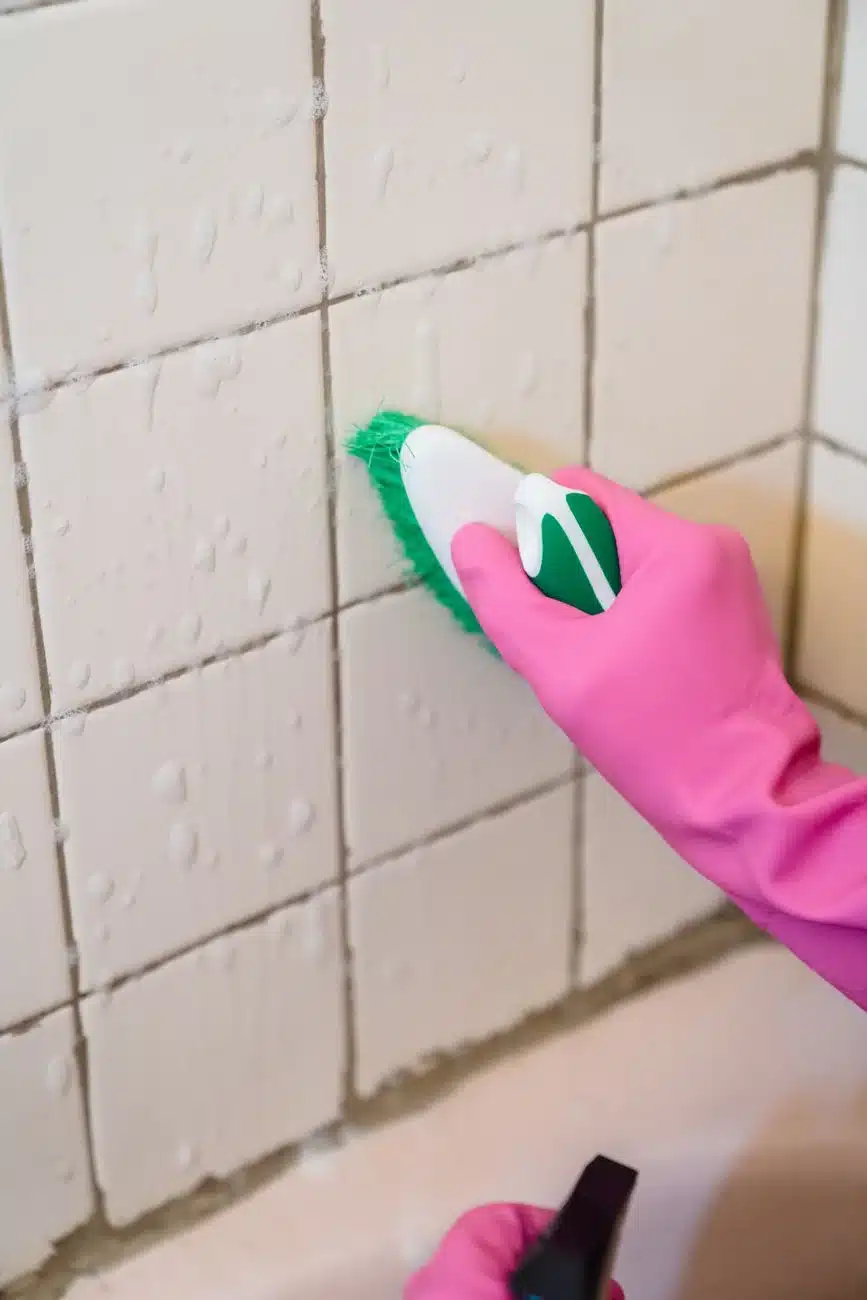 Hand scrubbing bathroom shower tiles with a cleaning brush - How to Deep Clean a Bathroom: A Room-by-Room Checklist