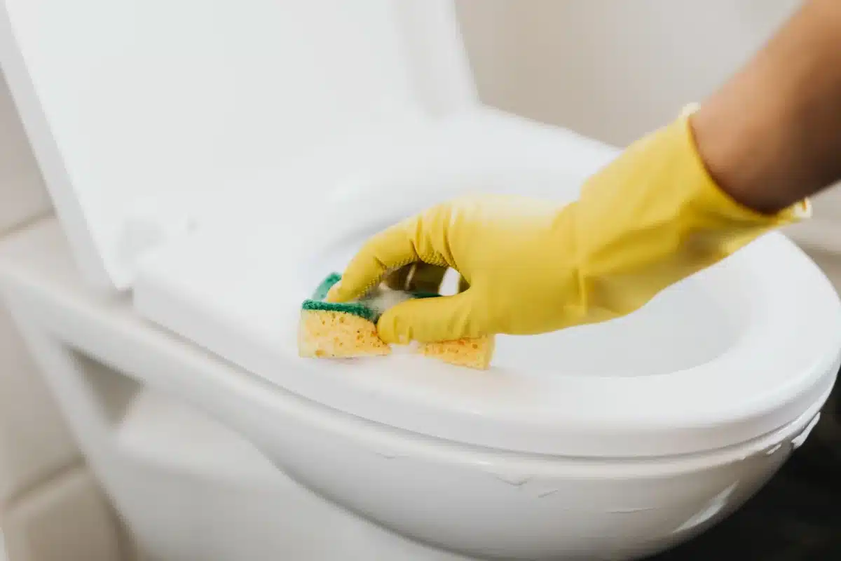 Person cleaning a toilet bowl with a soapy sponge wearing rubber gloves - How to Deep Clean a Bathroom: A Room-by-Room Checklist